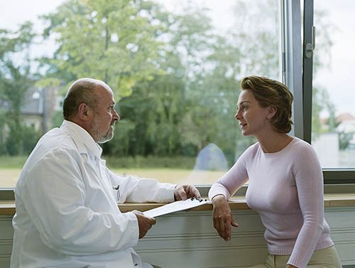 A caring doctor listening to a female patient's concerns, discussing her medical condition and treatment options in front of a window