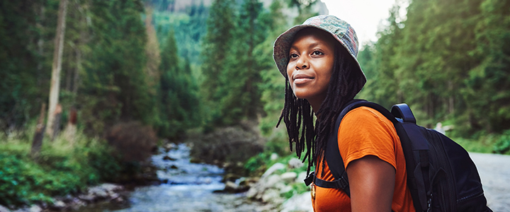 Photo of a woman with dark skin, hiking in a peaceful wooded area with a serene expression