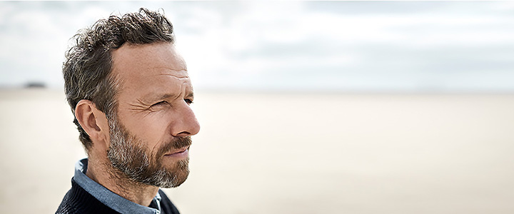 White man looking out across the sand on a beach, underscoring the need for patient-centered care and support in clinical trials