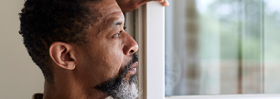 Middle aged African American man looking out a window thinking about his prostate cancer diagnosis and what his next steps will be